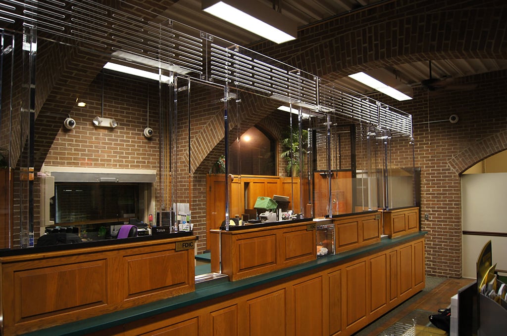  A photo showing a teller line outfitted with bullet proof glass as a protective shield from attempted attacks while maintaining high-optical clarity for customer interactions