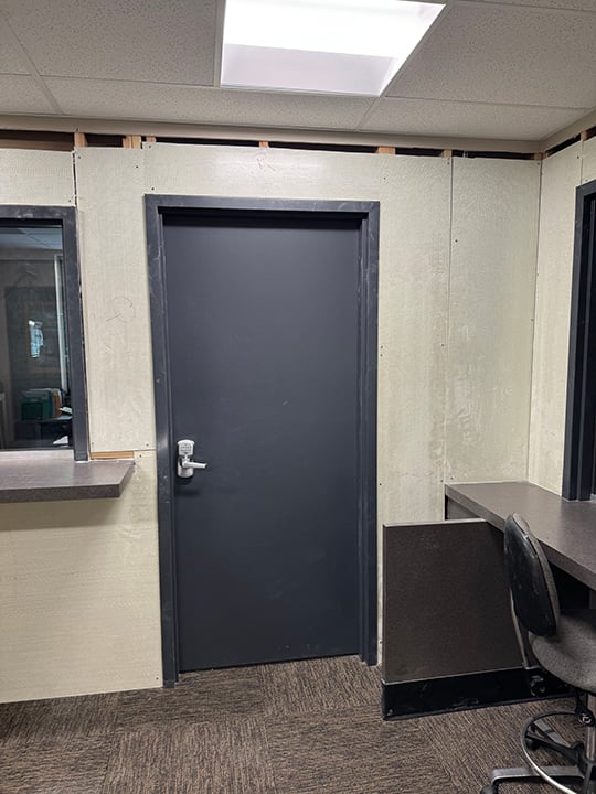 An example of a single bullet proof steel door installed in the interior wall of a building and constructed to fit in with the aesthetics of the space